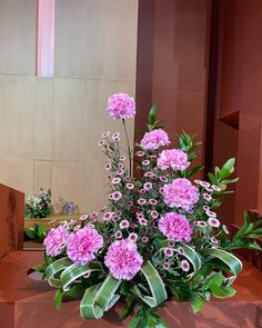 a bouquet of pink carnations and greenery in a vase on a table