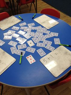 a blue table topped with lots of cards on top of wooden floor next to red chairs