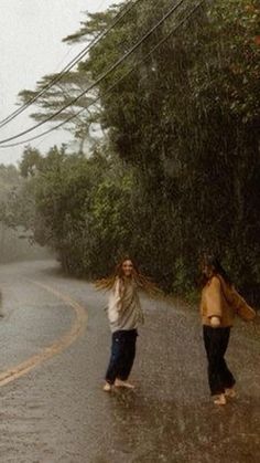 two people walking in the rain on a road with trees and power lines above them