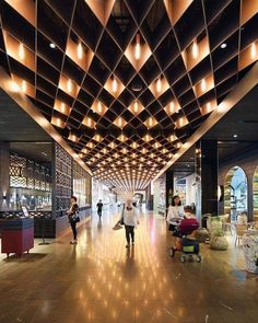 people are walking through an airport lobby with lights on the ceiling and wood flooring