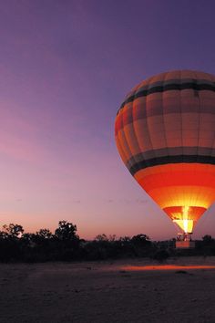 a hot air balloon is lit up in the sky at night with purple and orange hues