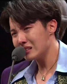 the man is speaking into his microphone while wearing a blue shirt and purple vest with gold accents