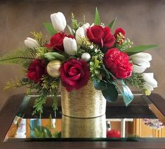 a vase filled with red and white flowers on top of a glass table next to a mirror