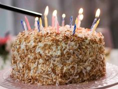 a cake that has some candles on it and is frosted with coconut flakes