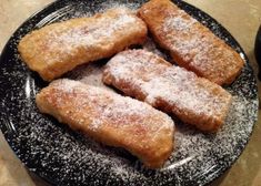 some type of dessert on a black plate with sugar sprinkled around the edges