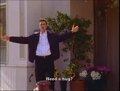 a man in a suit and tie standing on a porch with his arms outstretched, saying need a hug?