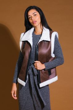 A faux leather/sherpa vest with high neckline and front buckle/zipper closure Details: Self : 100% PolyesterContrast 1 : 100% PolyesterContrast 2 : 100% Polyeurethane Size & Fit - Model is 5`8" And Wearing Size Small- Measurements Taken From Size Small- Approx. Length: 24" Trendy Winter Vest With Zipper Closure, Trendy Fall Vest With Zipper Closure, Sleeveless Outerwear With Zipper For Fall, Brown Sleeveless Vest With Faux Fur Lining, Brown Faux Fur Trim Vest For Fall, Brown Vest With Faux Fur Trim For Fall, Sherpa Vest, In Another Life, Leather Vest