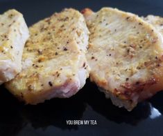 two pieces of meat sitting on top of a black plate with seasoning sprinkled on it