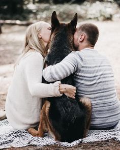 a man and woman sitting on a blanket with a dog in front of their face