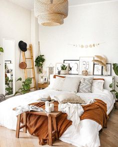 a bed with white sheets and pillows in a room filled with potted plants on the wall