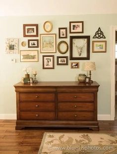 there is a dresser in the room with many framed pictures on the wall above it