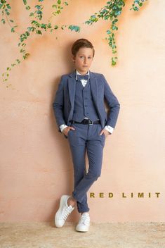 a boy in a suit leaning against a wall with his hands on his hips and wearing white shoes