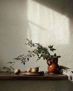 an orange vase and some pears on a wooden table next to a white wall