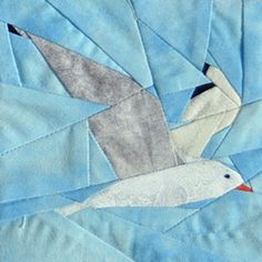 a bird is flying through the air on a blue quilted piece with grey and white designs