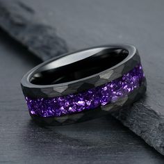 two wedding bands with purple stones inlayed to them on top of a rock