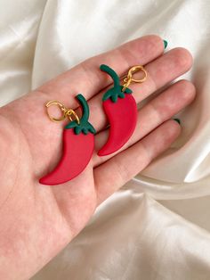 a hand holding two red and green earrings on it's palm, with gold chains