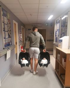 a man walking down a hallway carrying two baby strollers