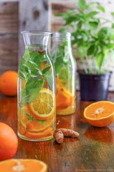 oranges, lemons and basil are in glass vases on a wooden table