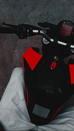 a red and black scooter parked next to a person's feet on the ground