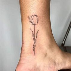 a small flower tattoo on the ankle that is black and white with a single tulip