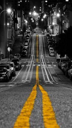 an empty city street at night with cars parked on both sides and yellow lines painted on the road