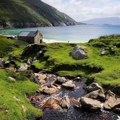 a stream running through a lush green hillside next to a small house on top of a hill