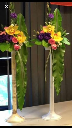 two tall vases with flowers and greenery in them