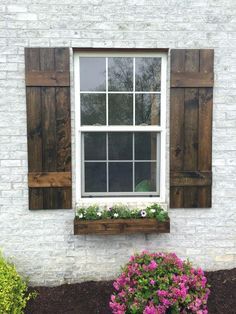 a white brick building with wooden shutters and flowers in the window box next to it