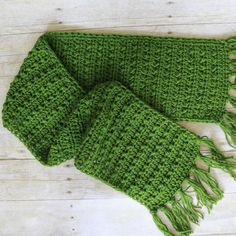 a green knitted scarf with fringes on a wooden surface