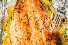 baked fish in foil with lemon slices and herbs on the side next to a fork