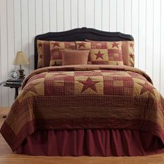 a bed with a red and brown quilted coverlet on top of it next to a night stand