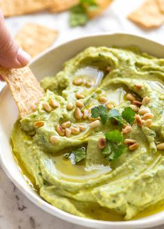 a person dipping guacamole into a bowl with crackers on the side