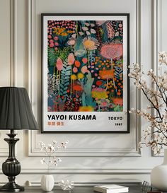 an art print hangs on the wall next to a lamp and vase with flowers in it