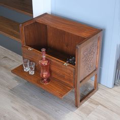 a small wooden cabinet with two glasses on the bottom and an empty bottle next to it