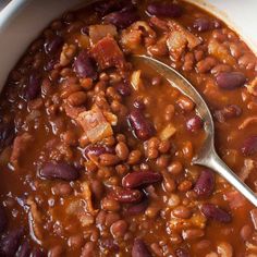 a bowl filled with beans and meat next to a spoon on top of a table