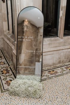 a mirror sitting on top of a tiled floor next to a building with a poem written in it