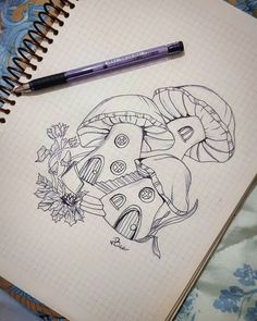 a notebook with a drawing of a mushroom house and flowers on the cover next to a pen