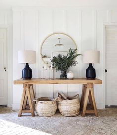 a wooden table topped with two lamps next to a mirror and vases on top of it