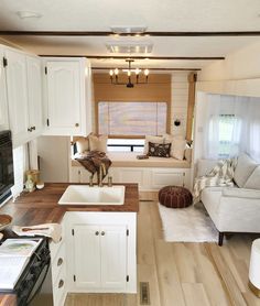 a kitchen and living room in a mobile home with white cabinets, wood flooring and an open window