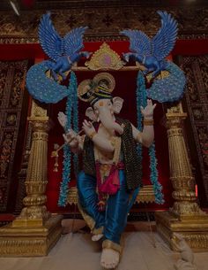 an elephant statue sitting in front of a red wall with blue decorations on it's head