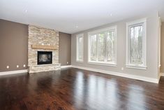 an empty living room with hard wood flooring and stone fireplace in the center area