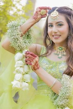 a beautiful young woman in a green dress holding flowers and wearing an elaborate head piece