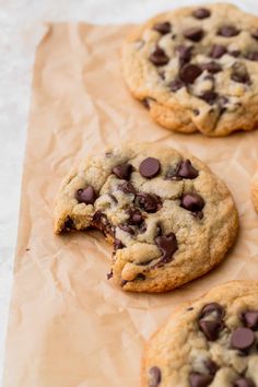 three chocolate chip cookies sitting on top of brown paper