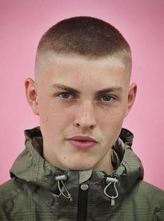 a young man with a shaved head wearing a green jacket