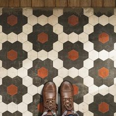 a person wearing brown shoes standing in front of a tiled floor with hexagonal tiles