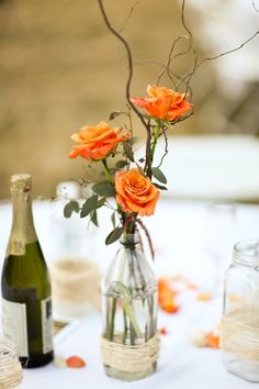 a vase filled with orange flowers sitting on top of a table next to two bottles