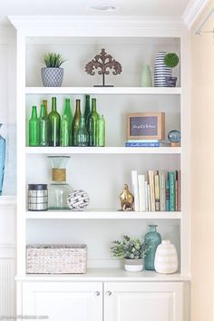 a white book shelf filled with lots of green vases and books on top of it