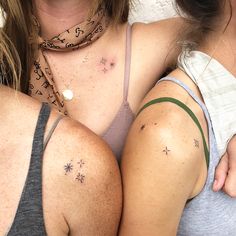 two women with tattoos on their arms and chest, one holding the other's shoulder