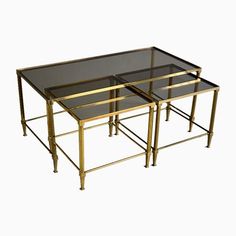 three glass and brass nesting tables with metal legs, one on each side holding a black top