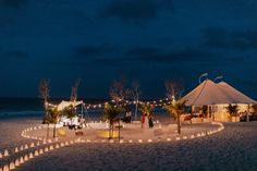 a tent set up on the beach at night with lights strung from it's poles